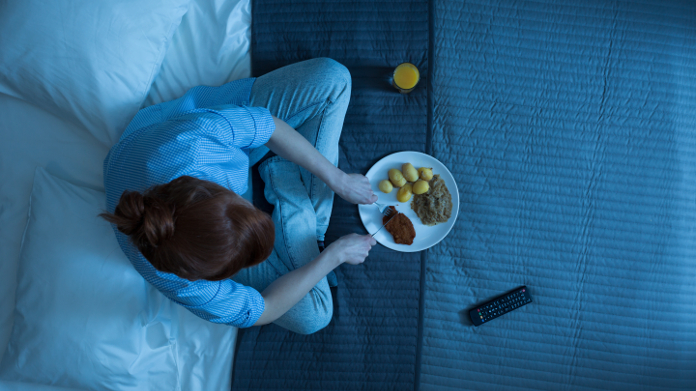 Frau, die nachts auf ihrem Bett isst