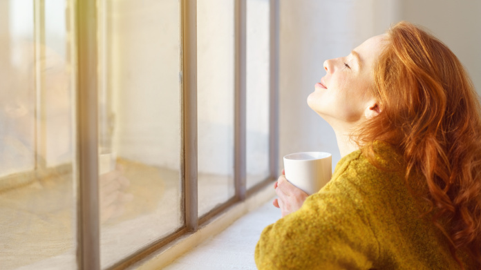 Junge rothaarige Frau beim Sonnenbaden hinter einem Fenster